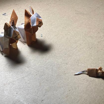 Two Siamese cats at the top left corner watch a mouse at bottom-right