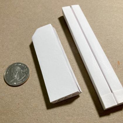 Two different kazoos folded from index cards next to a quarter for reference
